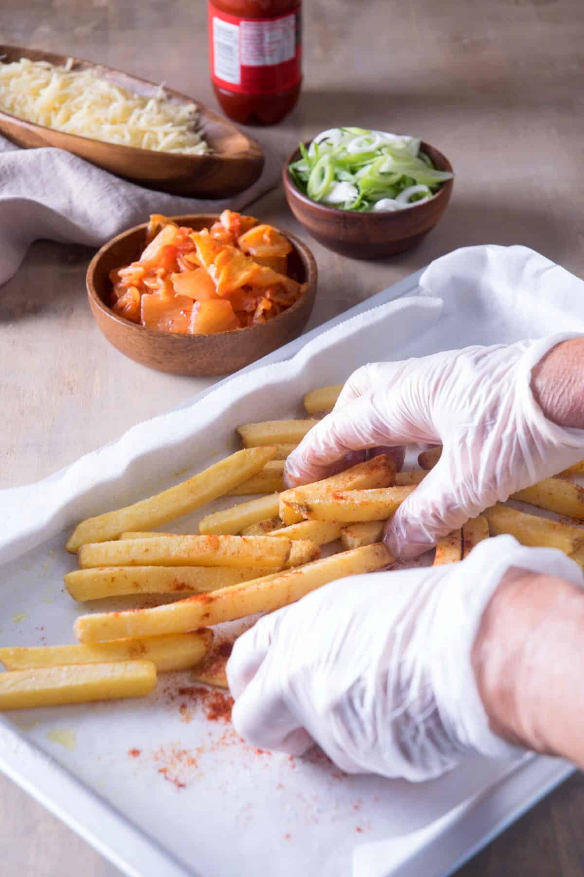 Fries with paprika on a baking sheet. Hands with gloves are handling the fries.