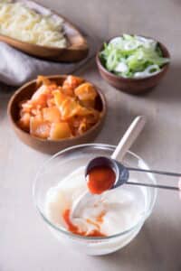 Small bowls with creamy sriracha sauce, shredded cheese, kimchi and sliced scallions on light background.