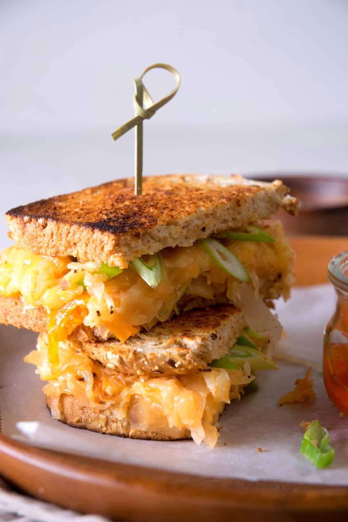 Kimchi grilled cheese sandwiches stacked on a brown plate with skewer.