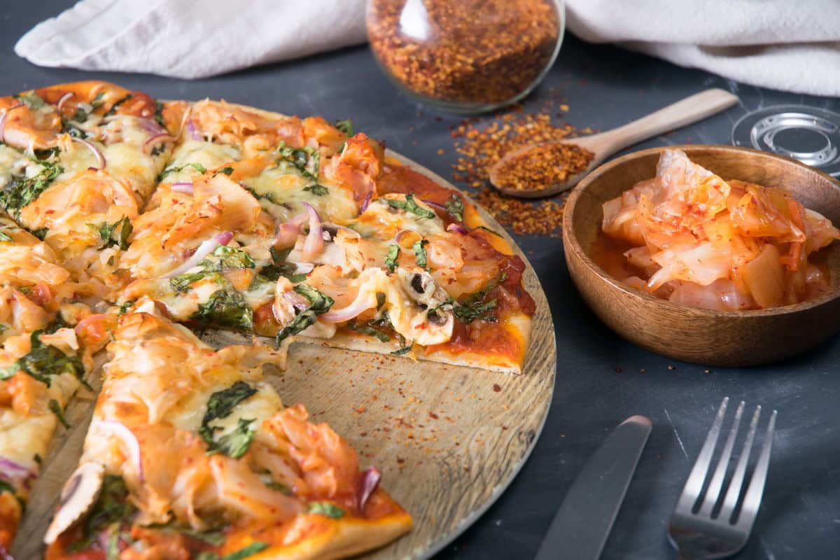 Sliced kimchi pizza on circular wooden cutting board.