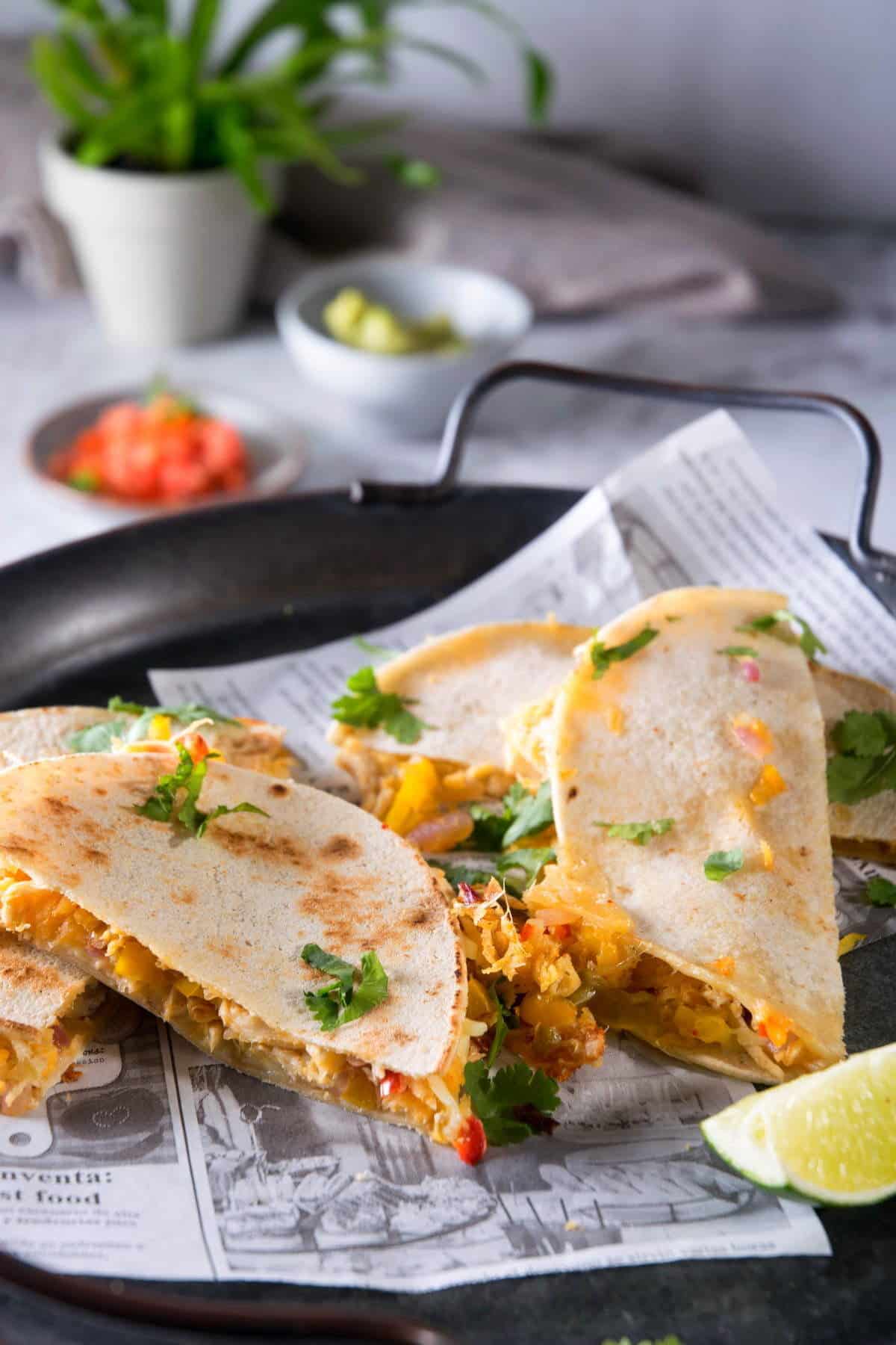 Kimchi quesadillas sliced on black serving tray with a lime wedge.
