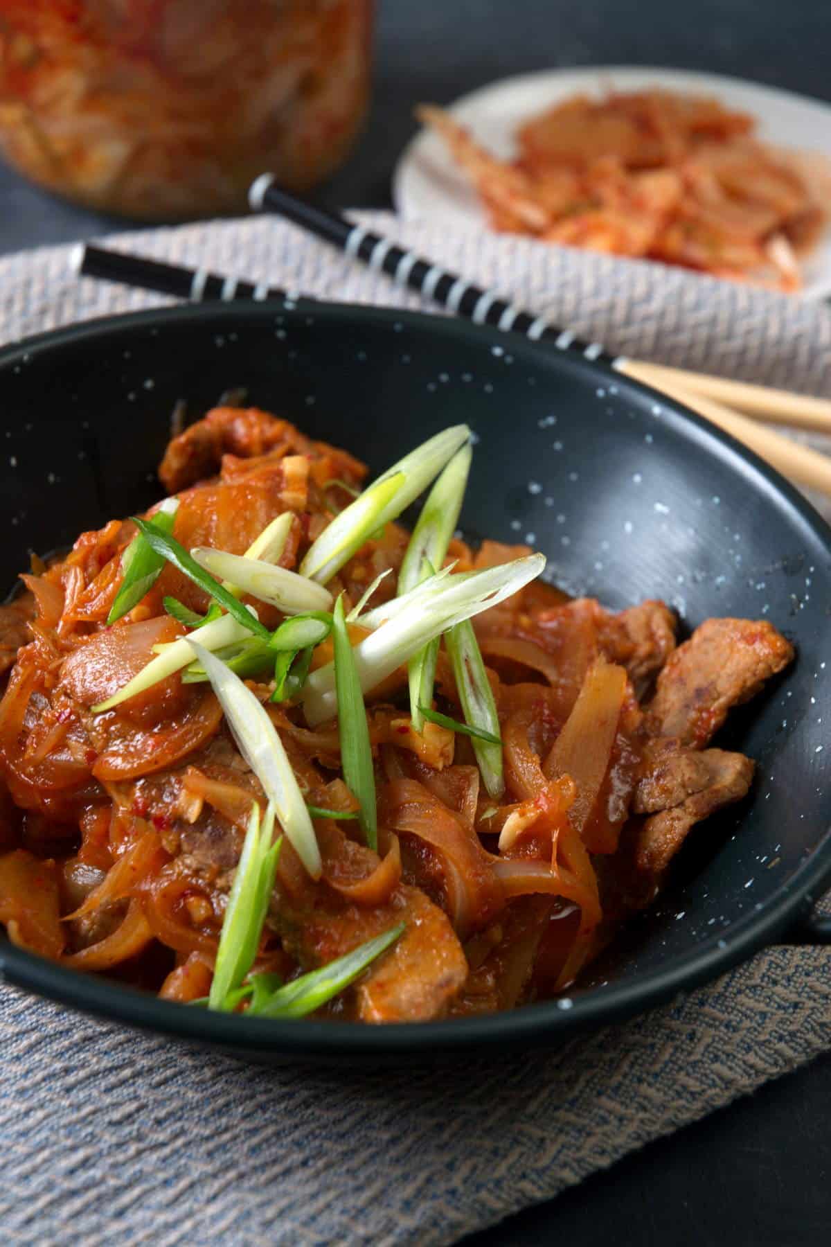 Kimchi stew in a black bowl with sliced scallions.