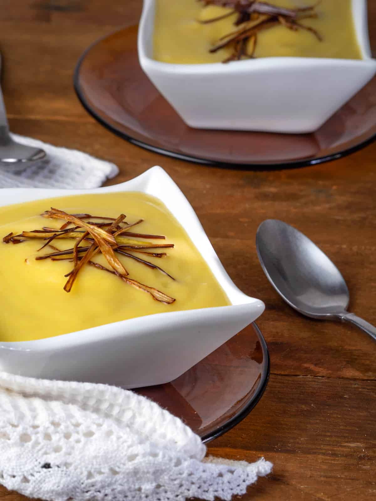 Leek and potato soup in white square soup bowls on wooden background.