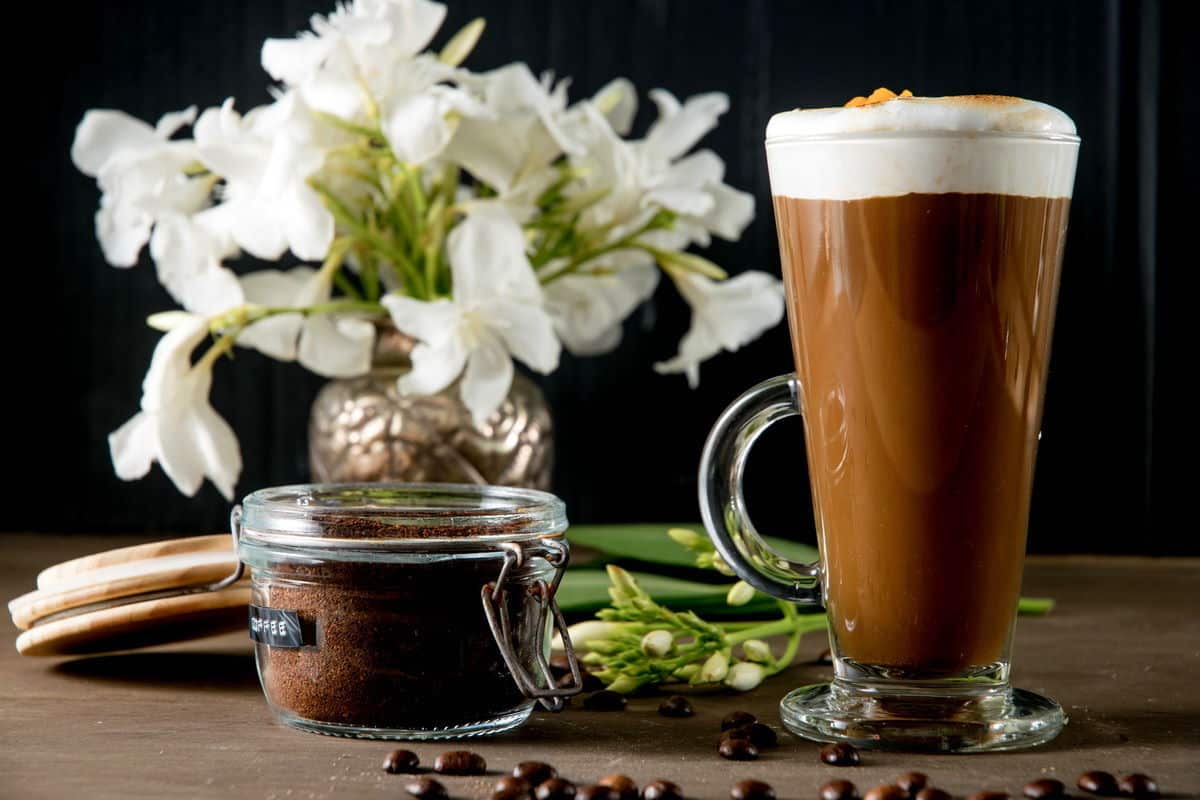Marshmallow pumpkin latte in a mug, coffee grind on the side and white flowers in the background.