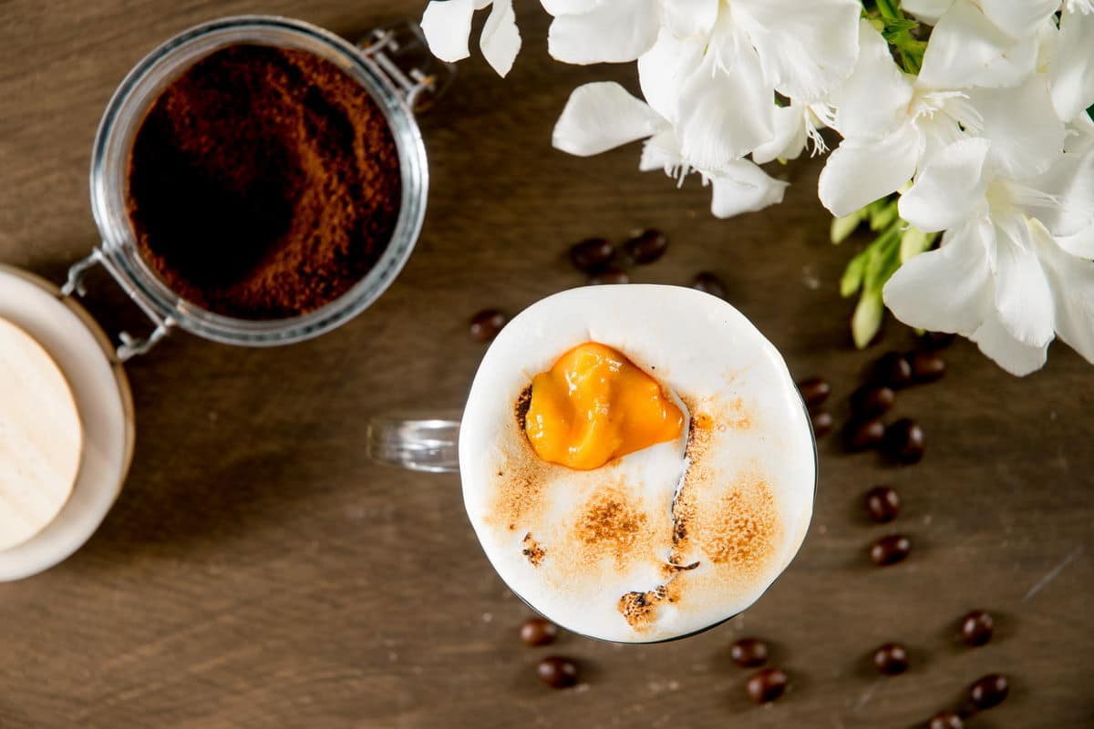 Marshmallow pumpkin latte in a mug, coffee grind on the side.