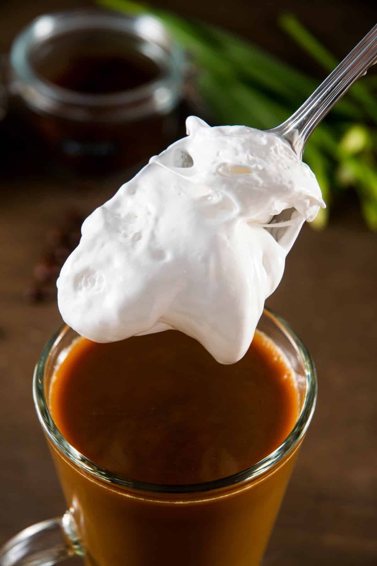 Marshmallow fluff on a spoon and a mug of pumpkin spice latte.