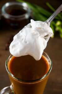 Marshmallow fluff on a spoon and a mug of pumpkin spice latte.