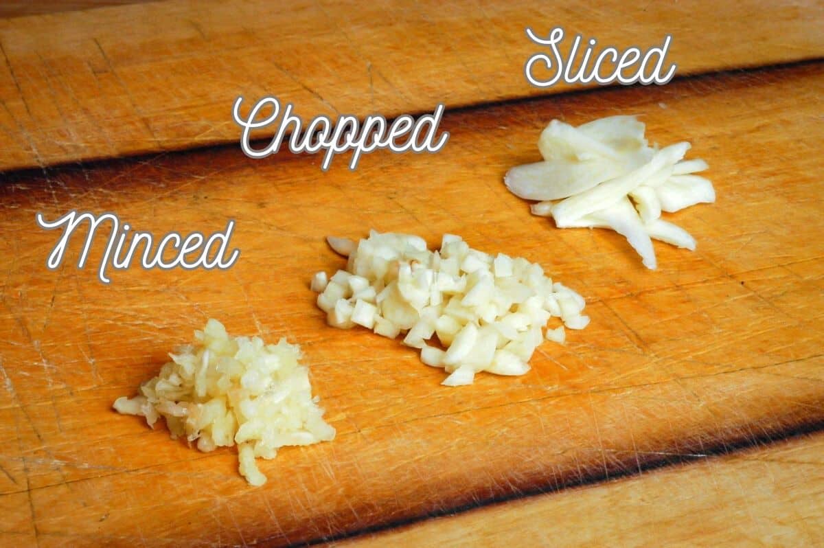 Minced, chopped and sliced garlic on wooden cutting board.