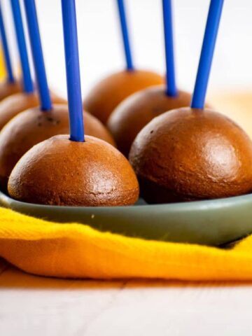 Naked chocolate cake pops on black dish with yellow cloth.