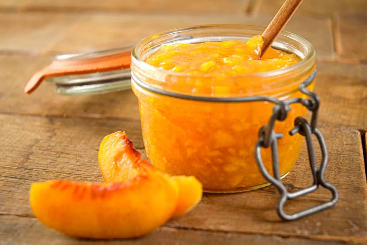 Peach freezer jam in a small jar with fresh peach slices on the side.