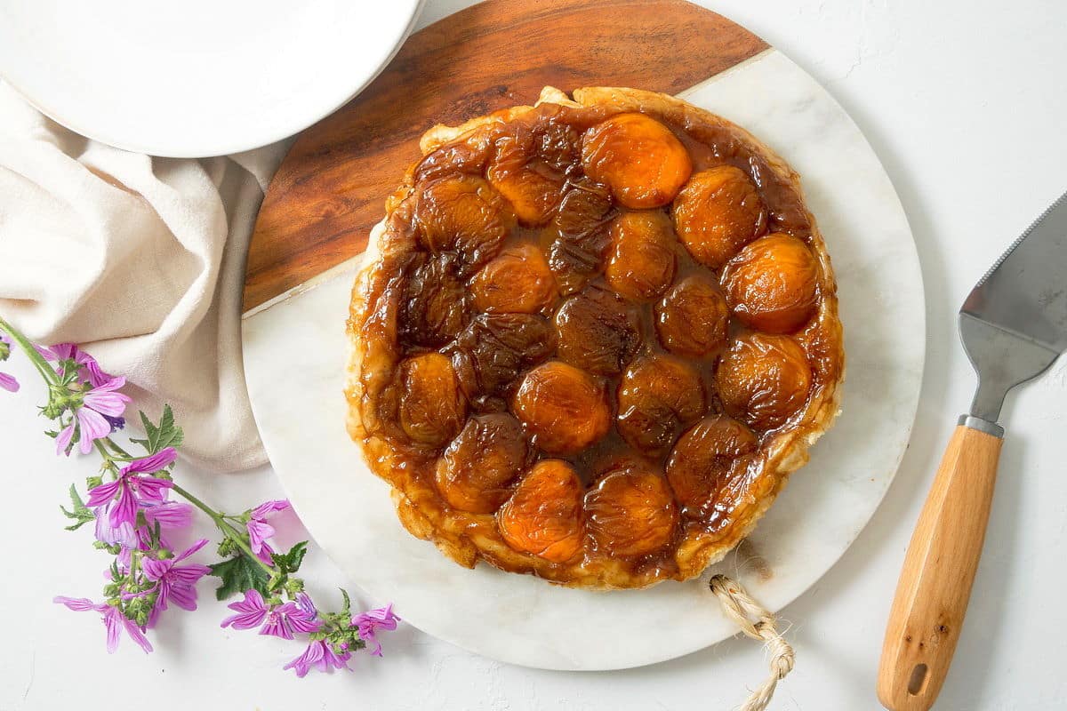 Peach Tarte Tatin on a marble and wooden serving board, purple flowers in the background.