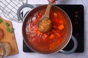 Peanut butter on spoon over soup in pot.