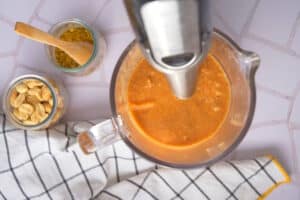 Peanut butter soup in jar with immersion blender, and peanuts on the side.