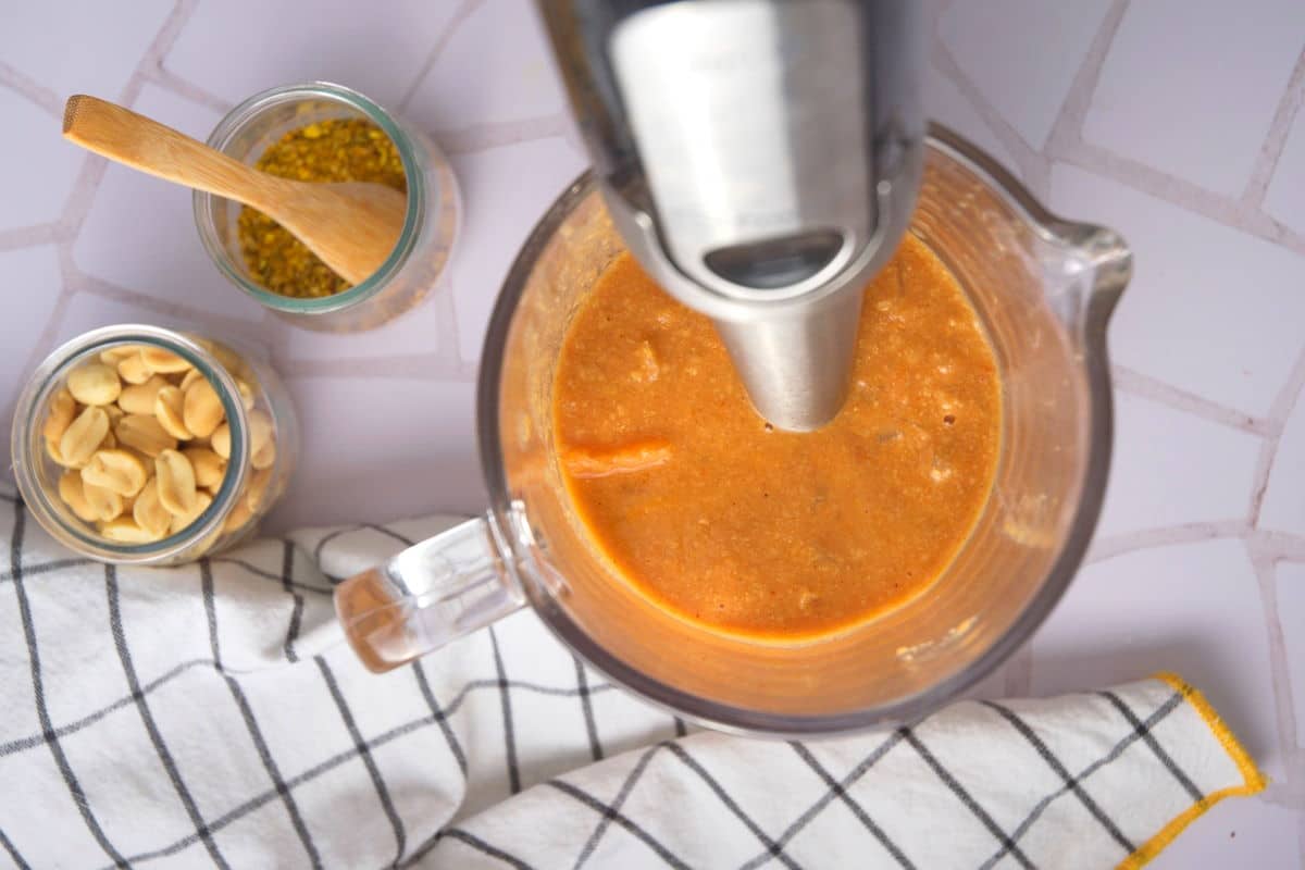 Peanut butter soup in jar with immersion blender, and peanuts on the side.