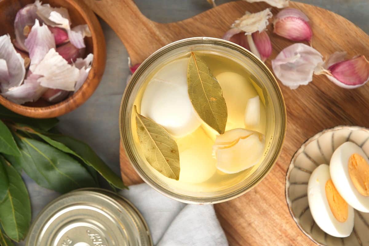 Pickled eggs in a glass jar with garlic cloves and bay leaves on the side.