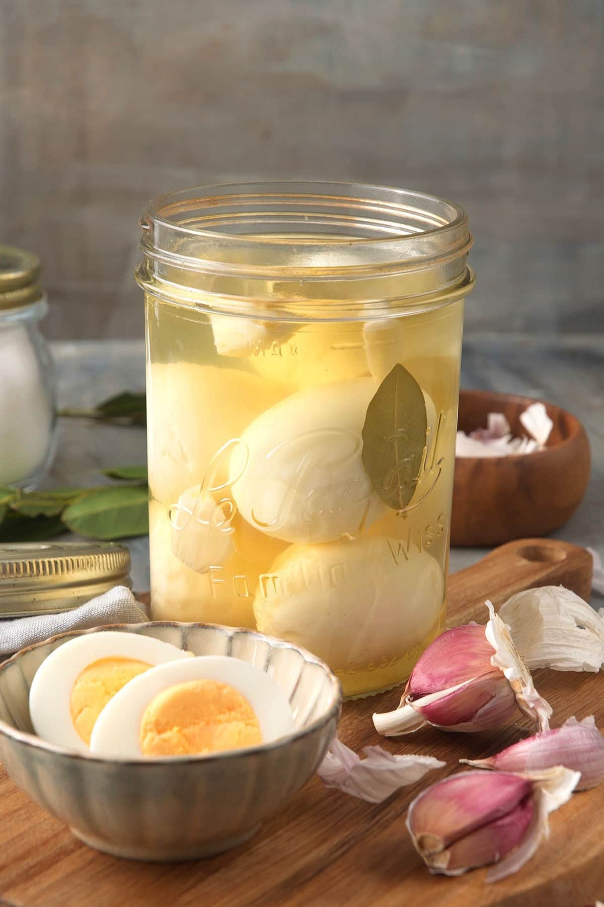 Pickled eggs in a glass jar with sliced egg and garlic cloves on the side.
