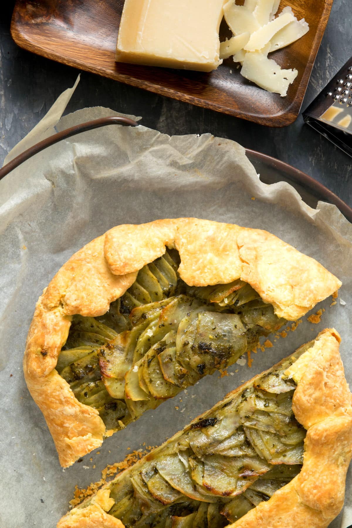 Potato galette sliced in half on parchment paper with Parmesan cheese block on the side.