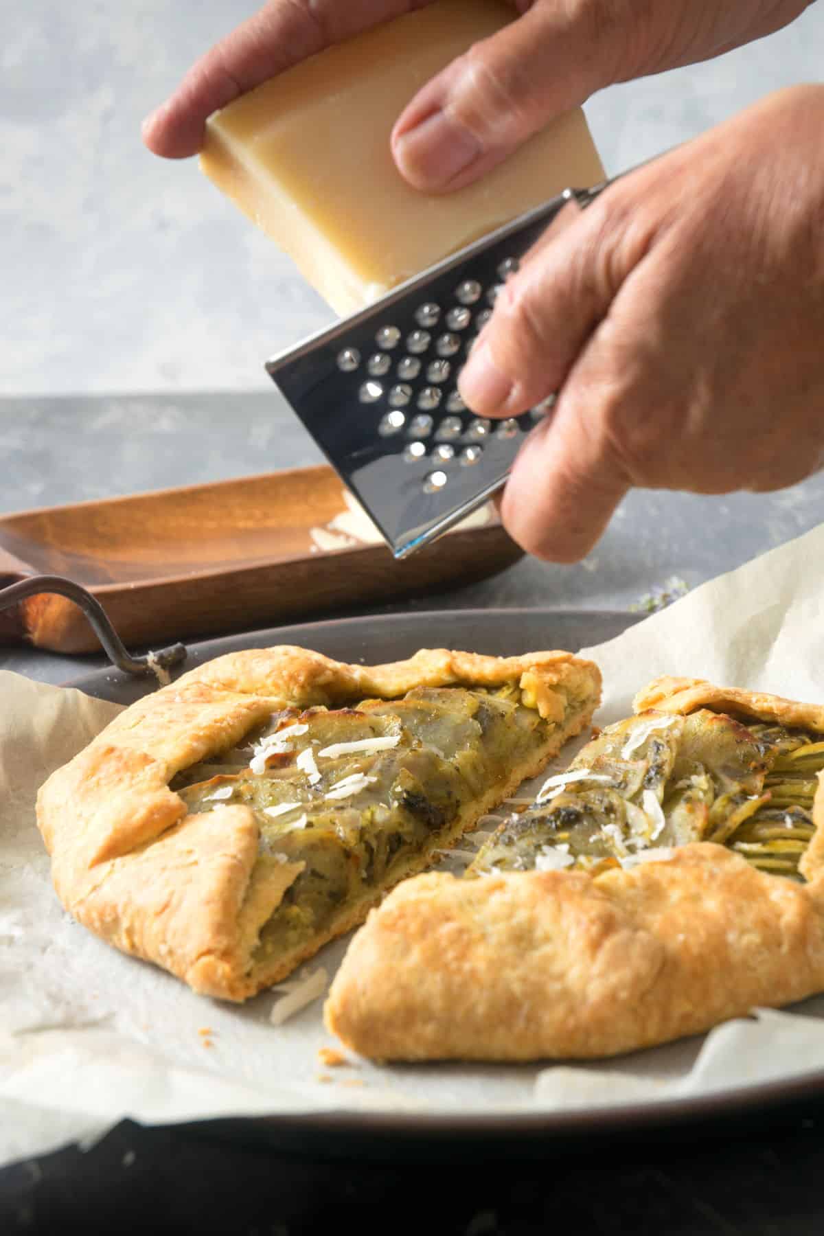 Parmesan grated over potato galette on parchment paper.