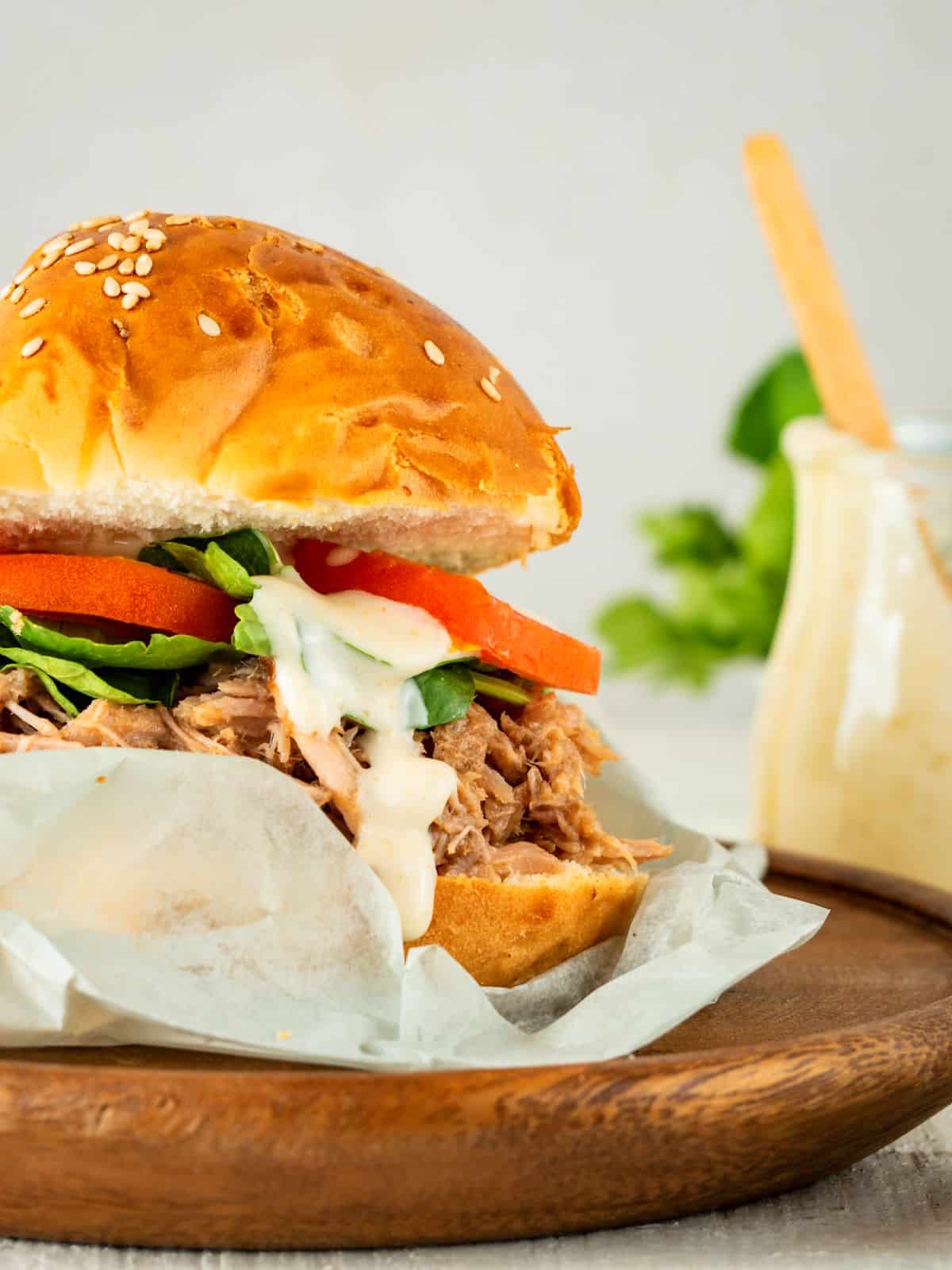 Pulled pork burger with special sauce on wooden plate.