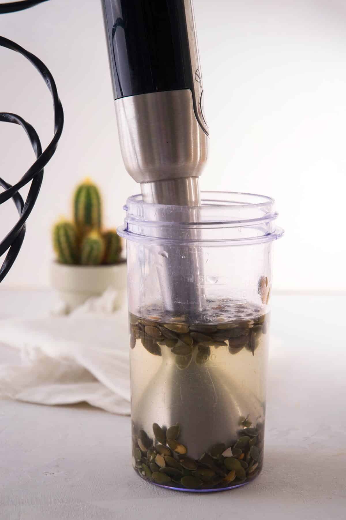 Pumpkin seeds and filtered water in a blender jar.