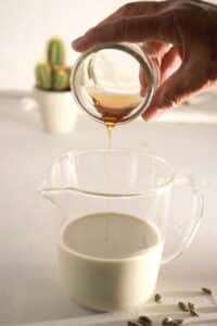 Agave nectar pouring into a measuring glass filled with pumpkin seed milk.