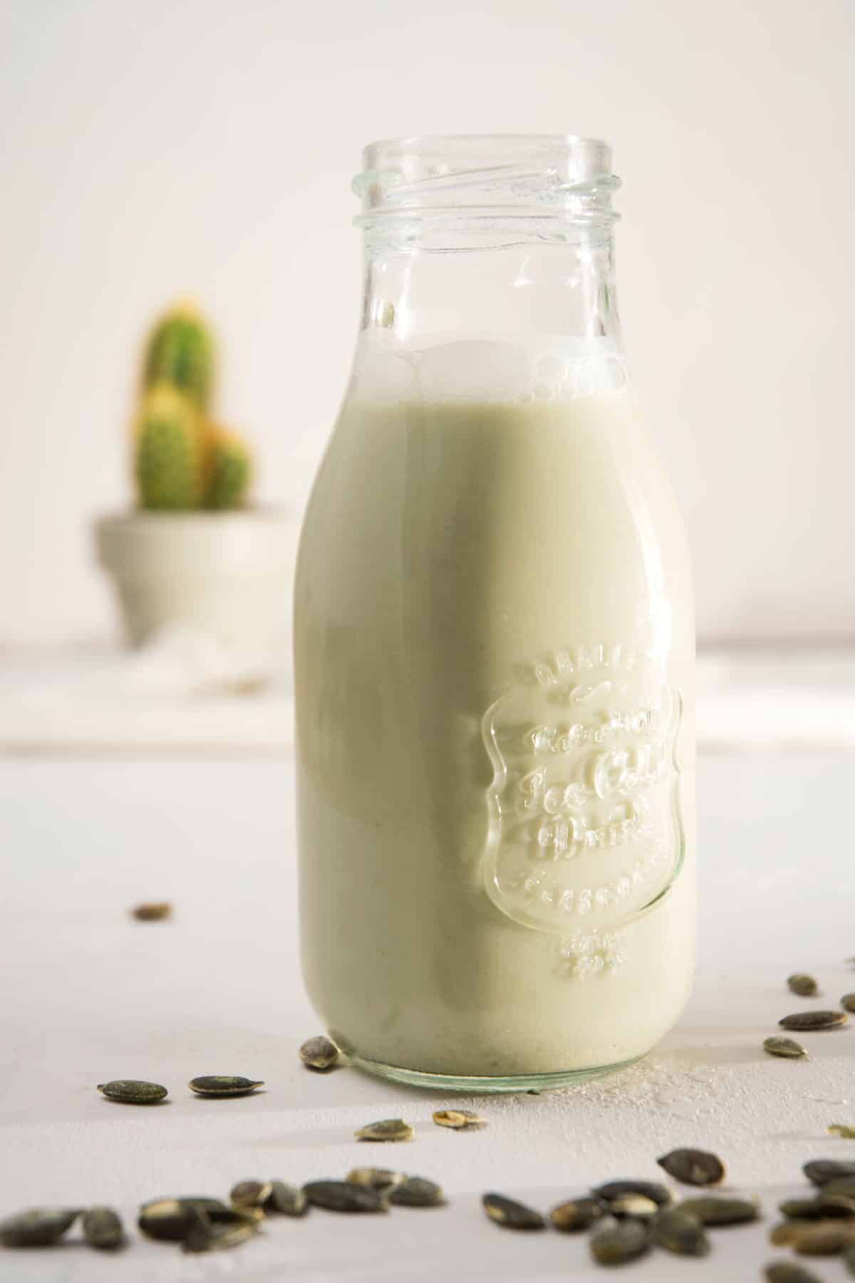 A jar of milk on light background, pumpkin seeds scattered around it.