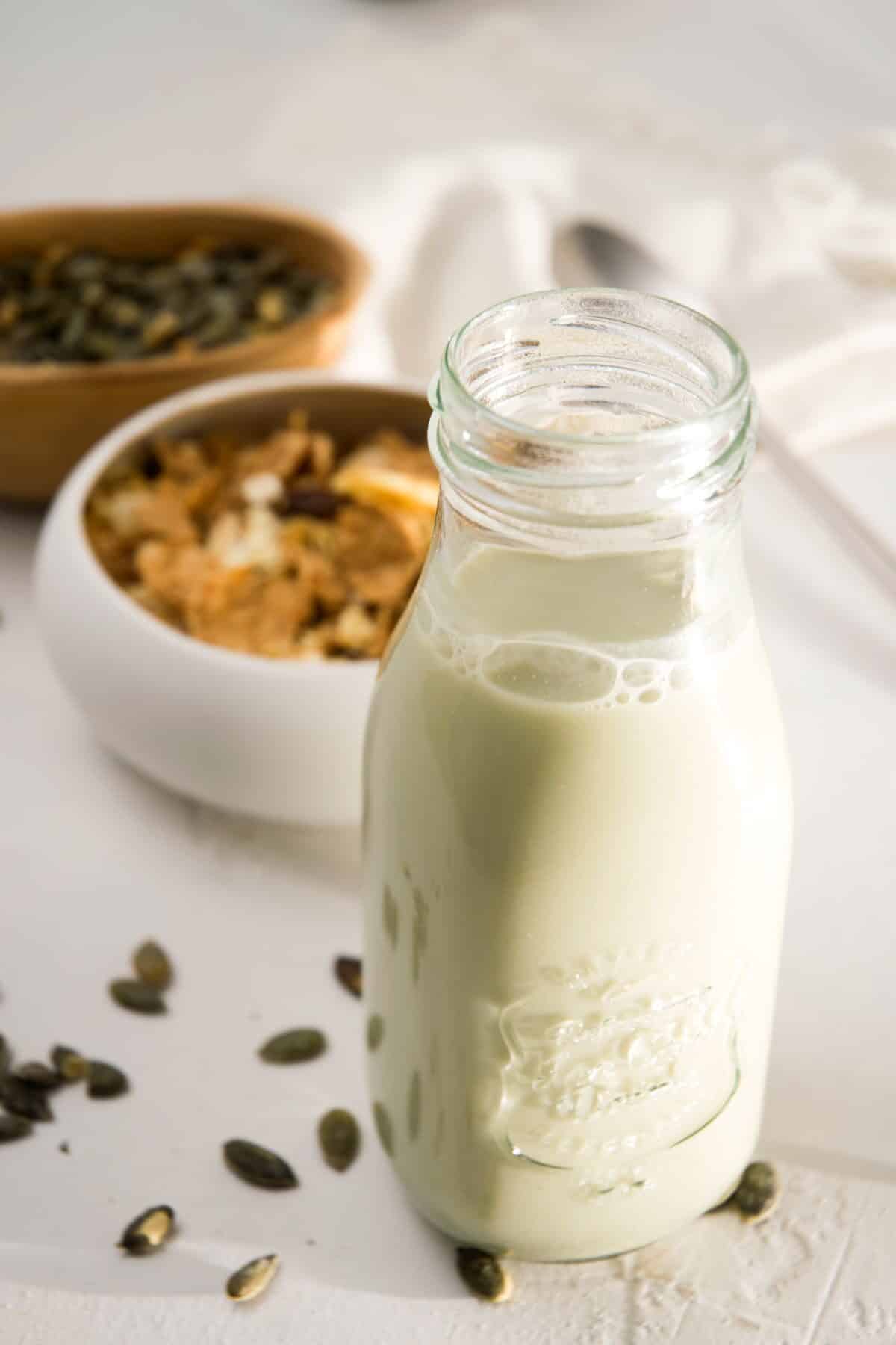 Pumpkin seed milk in a small jar on white background and pumpkin seeds in the background.