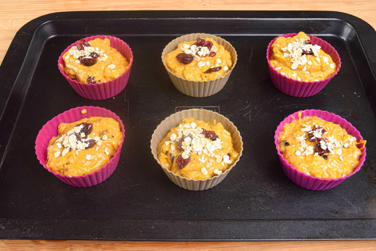 Unbaked pumpkin muffin matter in silicon molds on baking sheet.