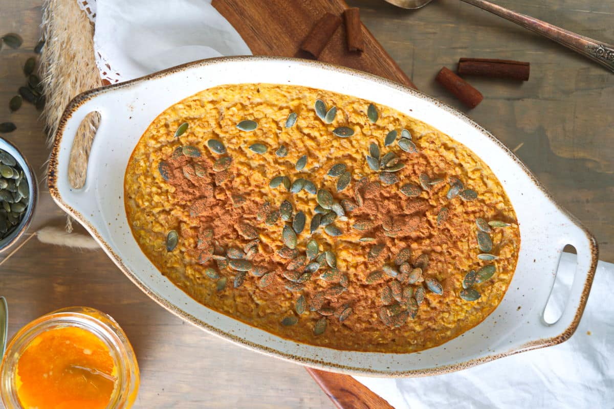 Pumpkin spice oatmeal in a white casserole dish on wooden cutting board.