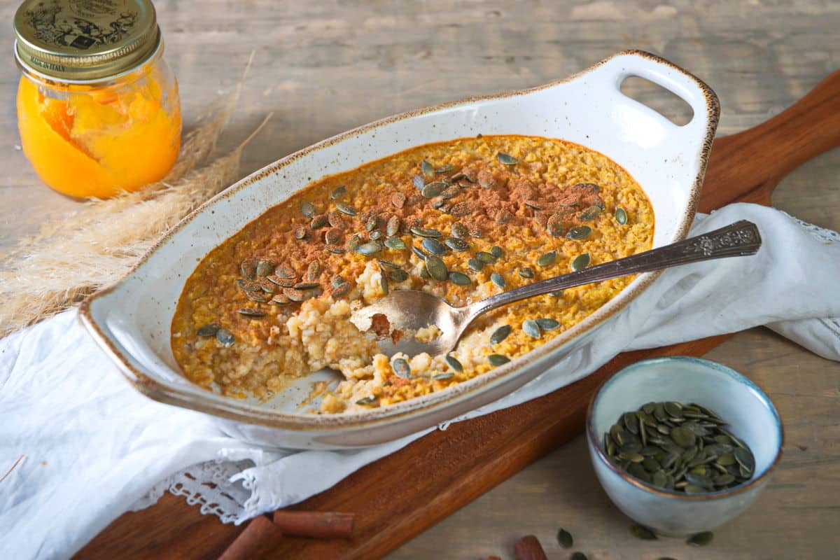 Pumpkin spice oatmeal in a white casserole dish with a spoon in it.