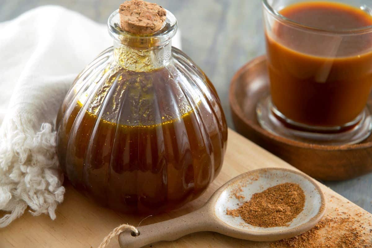 Pumpkin spice syrup in a small decorative jar, a spoon of pumpkin pie spice and a glass of pumpkin spice latte on the side.
