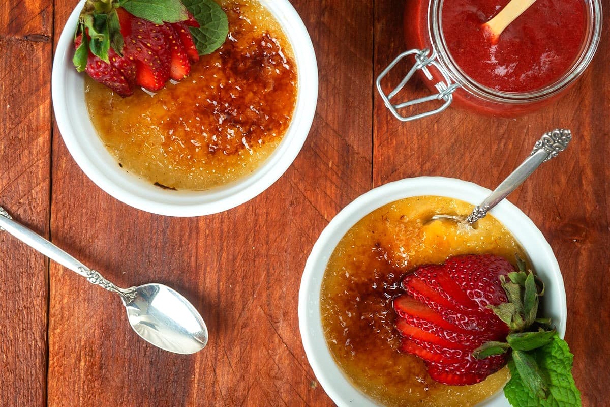 Raspberry Coulis Crème Brûlée in ramekins with spoons and coulis on the side.