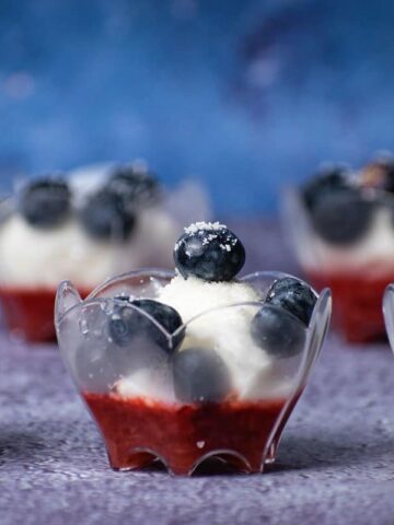 Ice cream and fruit dessert in mini dessert cups with blue background.