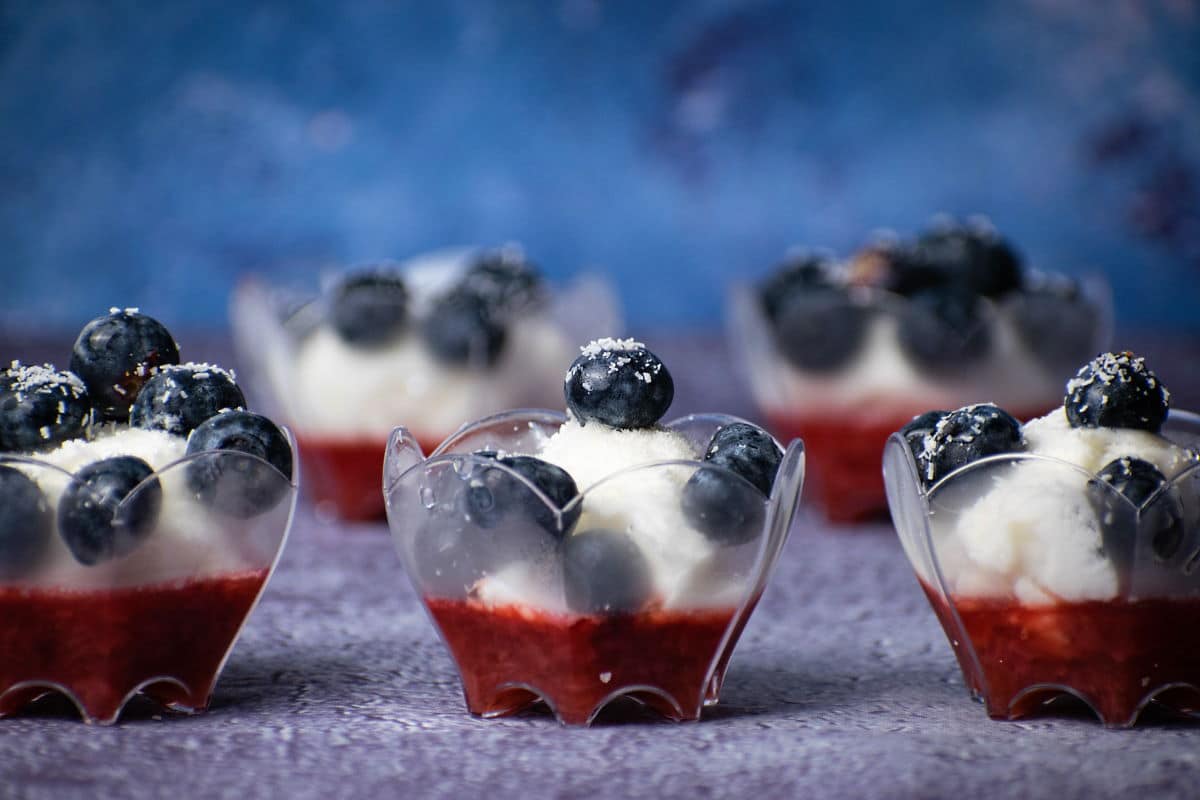 Ice cream and fruit dessert in mini dessert cups with blue background.
