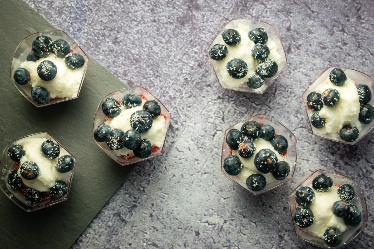 Top view of fruit and ice cream dessert in 6 mini dessert cups, blue background.