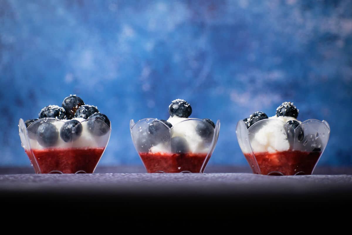 Fruit and ice cream in 3 mini dessert cups on blue background, front view.