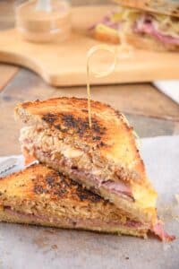 Reuben sandwiches stacked with a toothpick on parchment.