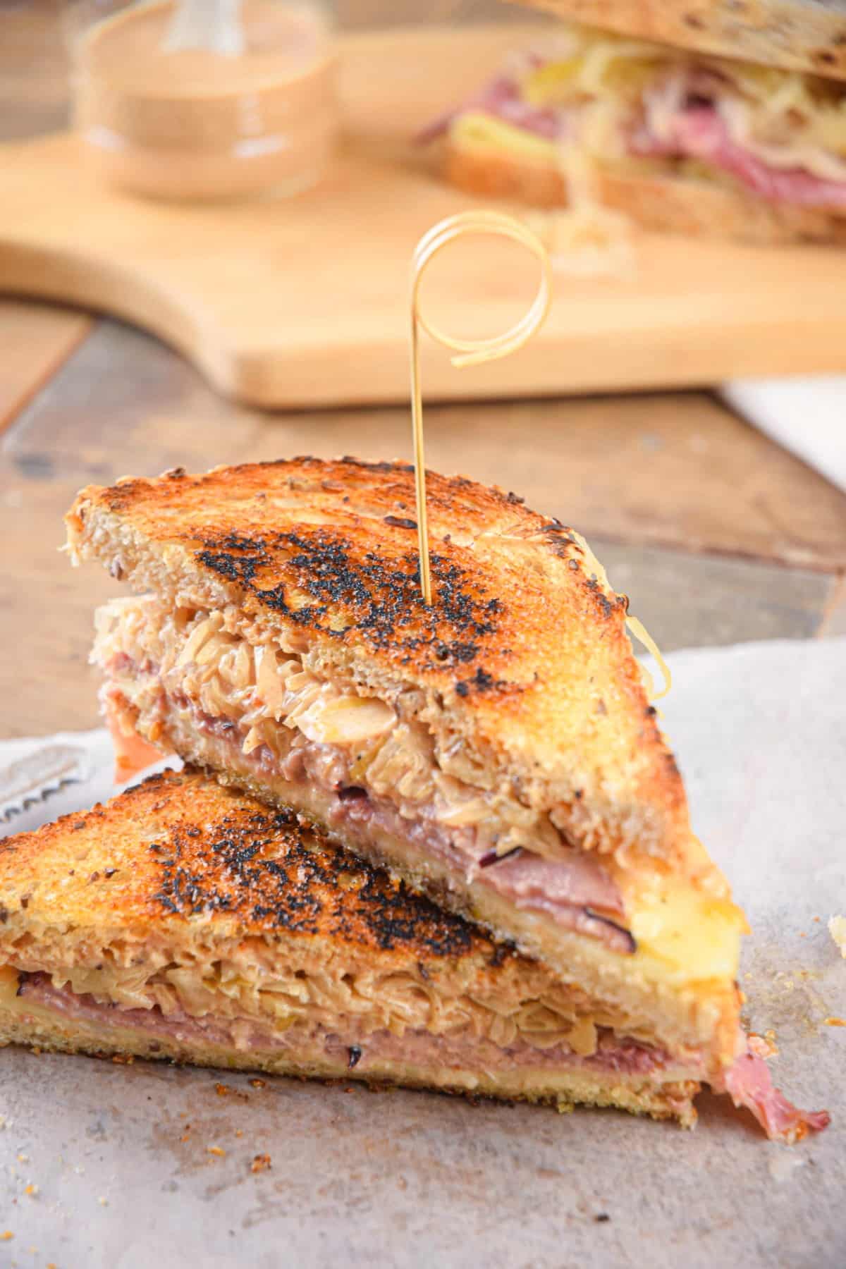 Reuben sandwiches stacked with a toothpick on parchment.