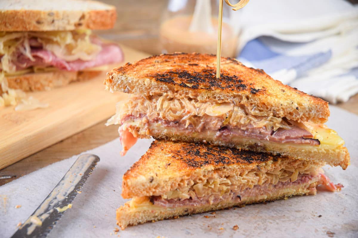 Reuben sandwiches stacked with a toothpick on parchment.