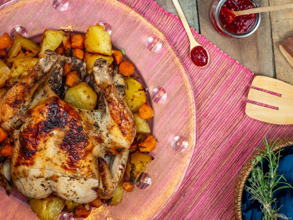 Roasted chicken stuffed with vegetables and herbs on plate with blackberry gravy on the side.