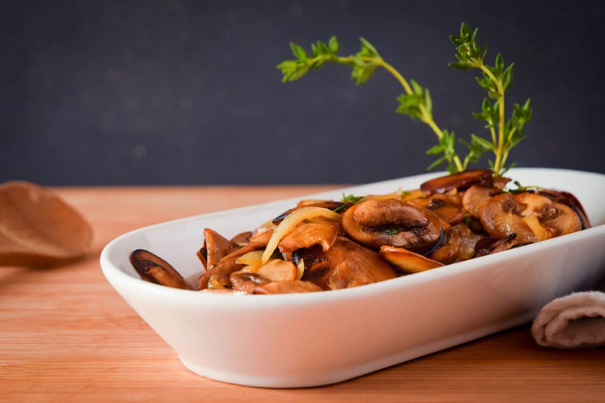 Sautéed mushrooms in white serving dish with fresh thyme.