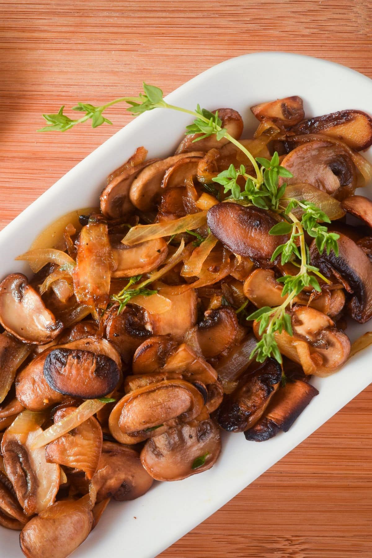 Sautéed mushrooms in white serving dish with fresh thyme.