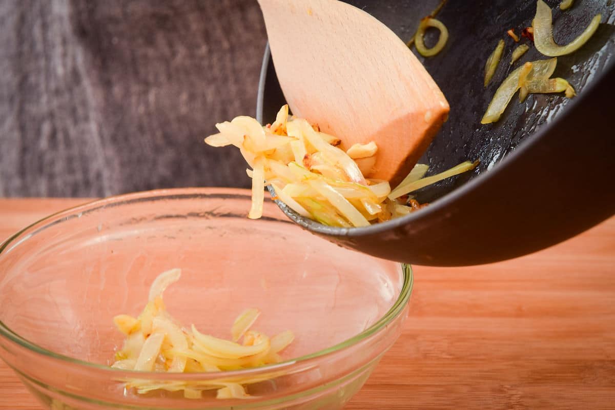 Sliced onions in pan and bowl with wooden spatula.