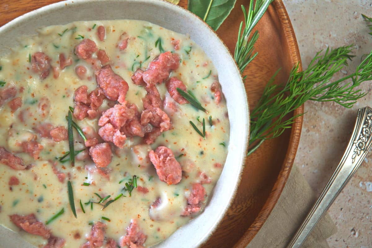 Sawmill gravy with fresh herbs in a white bowl over a wooden plate.