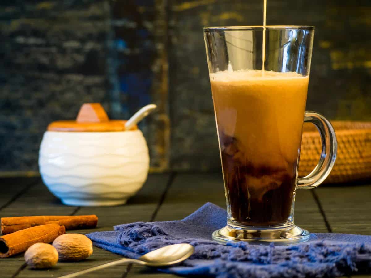 Simple Pumpkin Spice Coffee Cream Coffee cream pouring into a mug with cinnamon sticks and sugar jar in the background.
