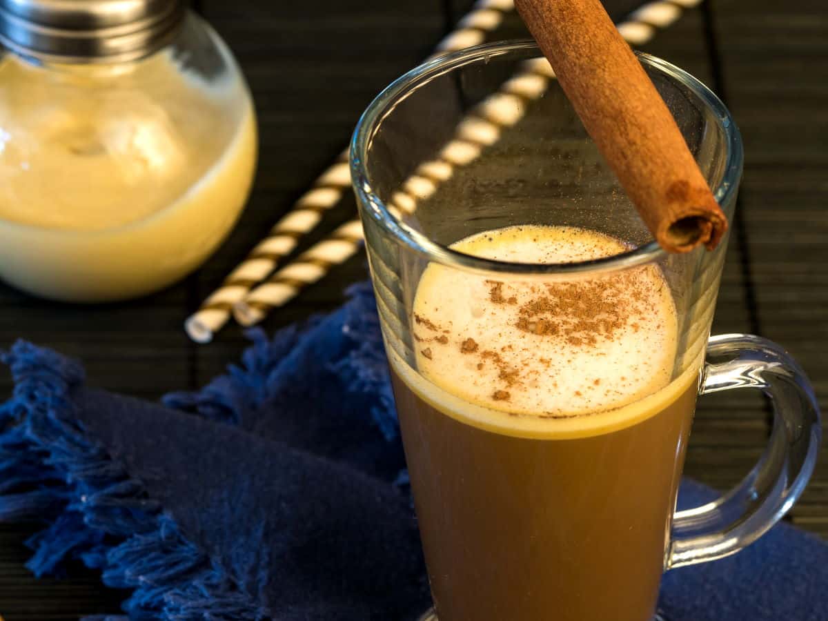 Coffee in a mug with a cinnamon stick and jar of pumpkin spice creamer.