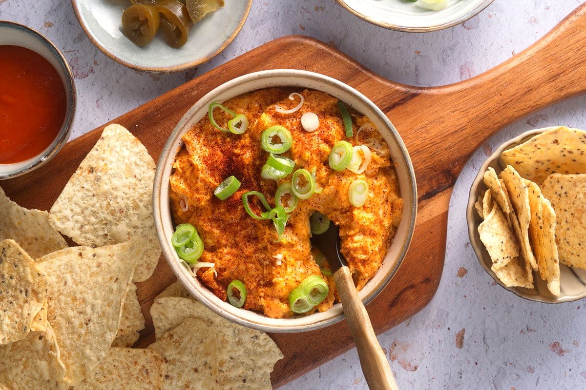 Buffalo chicken dip on wooden serving board and tortilla chips on the side.