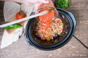 Diced vegetables and tomato passata in slow cooker with wooden spoon.