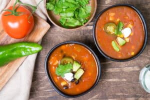 Mexican soup in black bowls, cilantro and a tomato on the side.