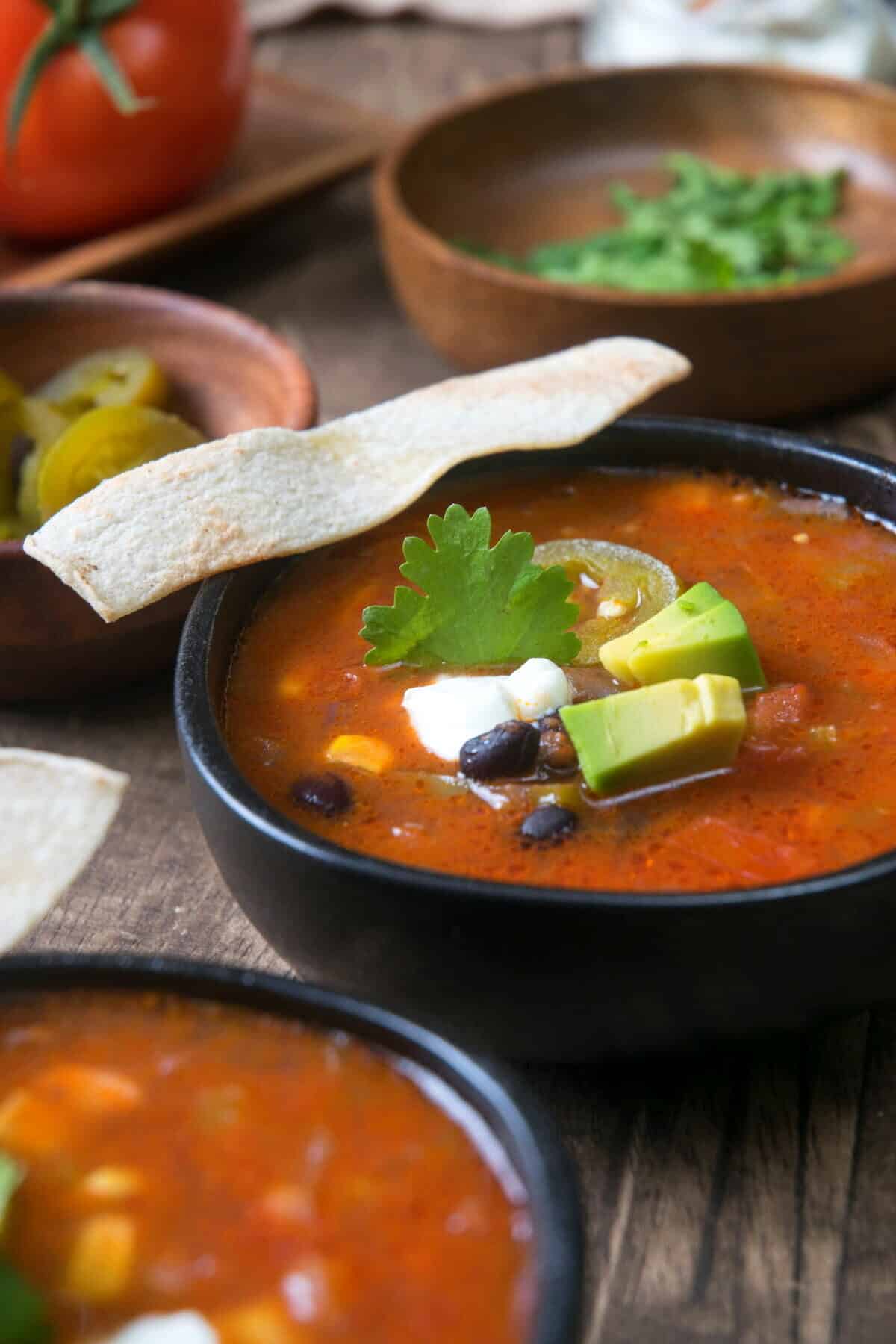 Mexican soup in black bowls with tortilla strips.